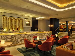 A bar area with a marble countertop, multiple seating options including red upholstered chairs, and a staircase leading to another level. - The Imperial (London)