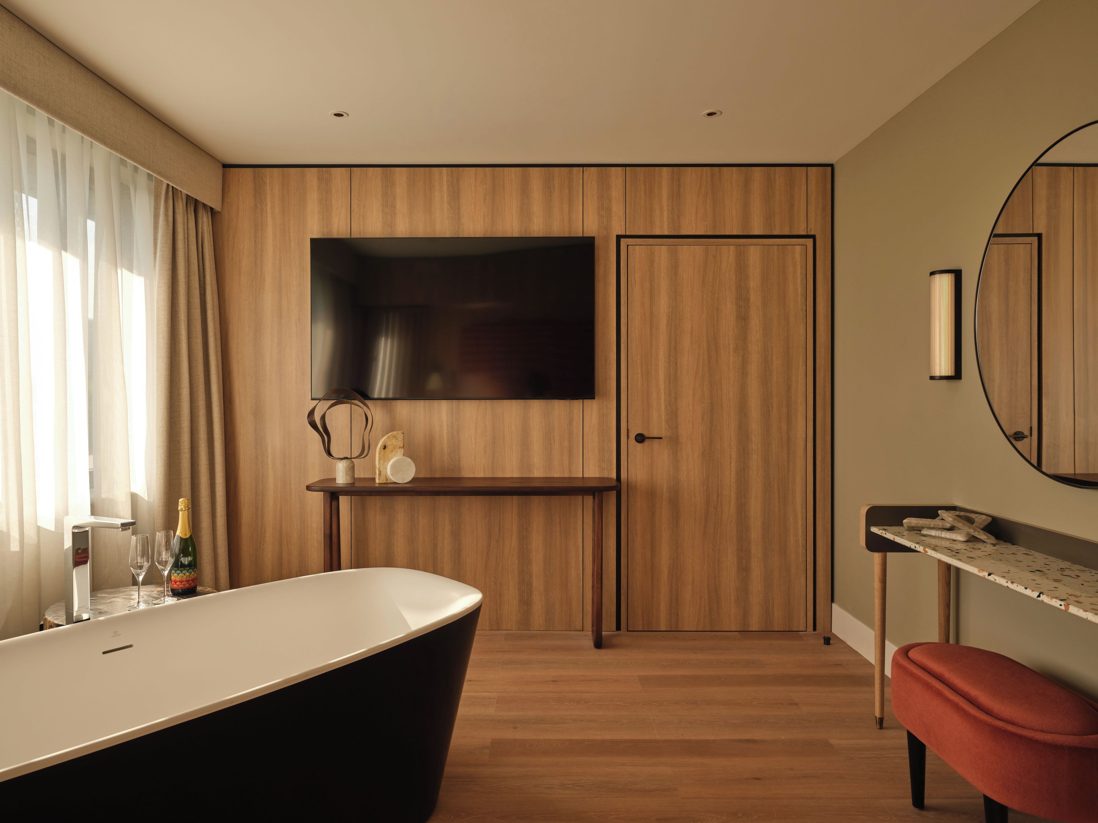 A modern bathroom with a freestanding bathtub, a vanity with a mirror, and a wooden panel wall.