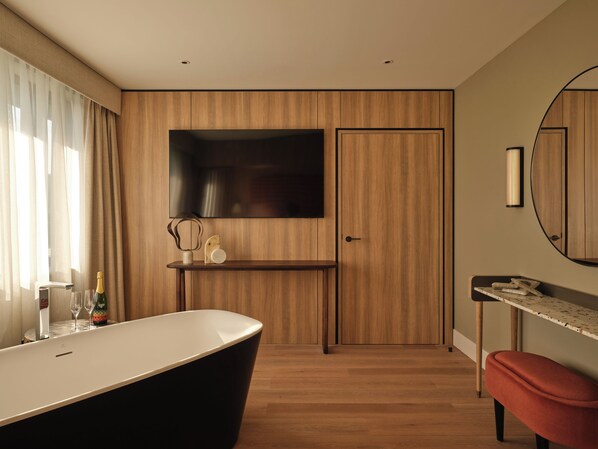 A modern bathroom with a freestanding bathtub, a vanity with a mirror, and a wooden panel wall. - The Imperial (London)