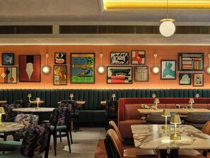 A restaurant interior with booths, round tables, and wall art. - The Imperial (London)