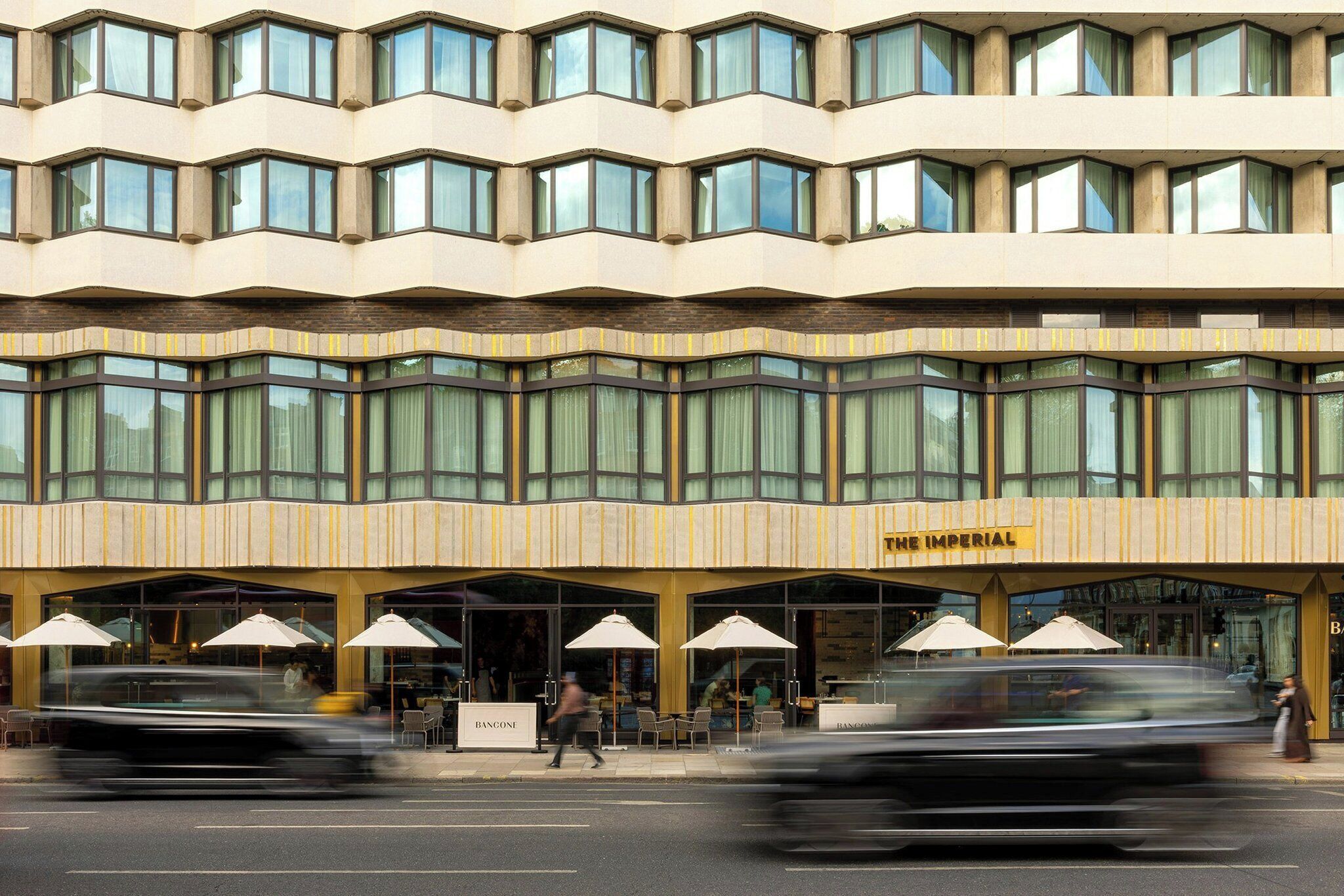 A hotel with a modern facade, multiple windows, and outdoor seating with umbrellas.