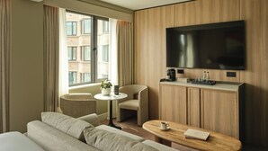 A hotel room with a large bed, a sofa, a small round table with a coffee maker, a TV on the wall, and a view of the city through the window. - The Imperial (London)