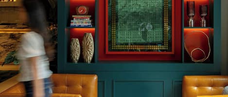 A modern interior with a central decorative rug, shelves with books and decorative items, and two leather armchairs.