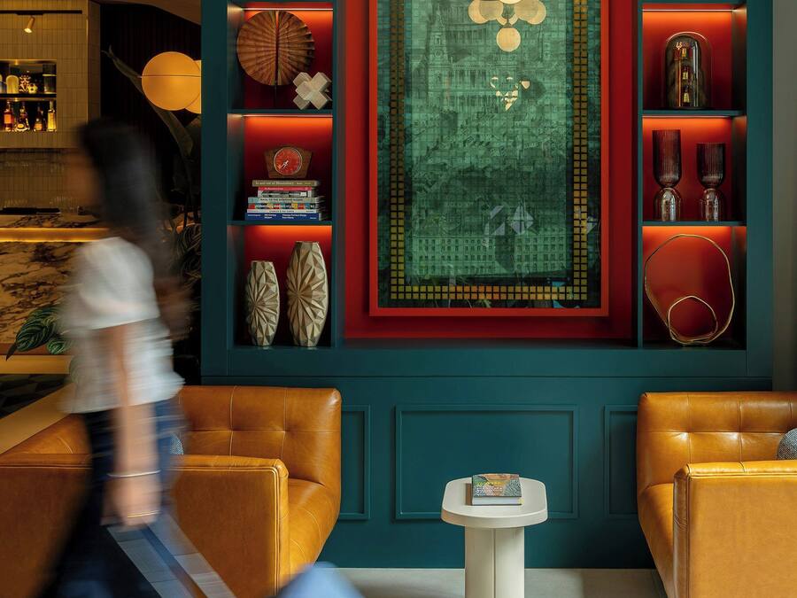 A modern interior with a central decorative rug, shelves with books and decorative items, and two leather armchairs.
