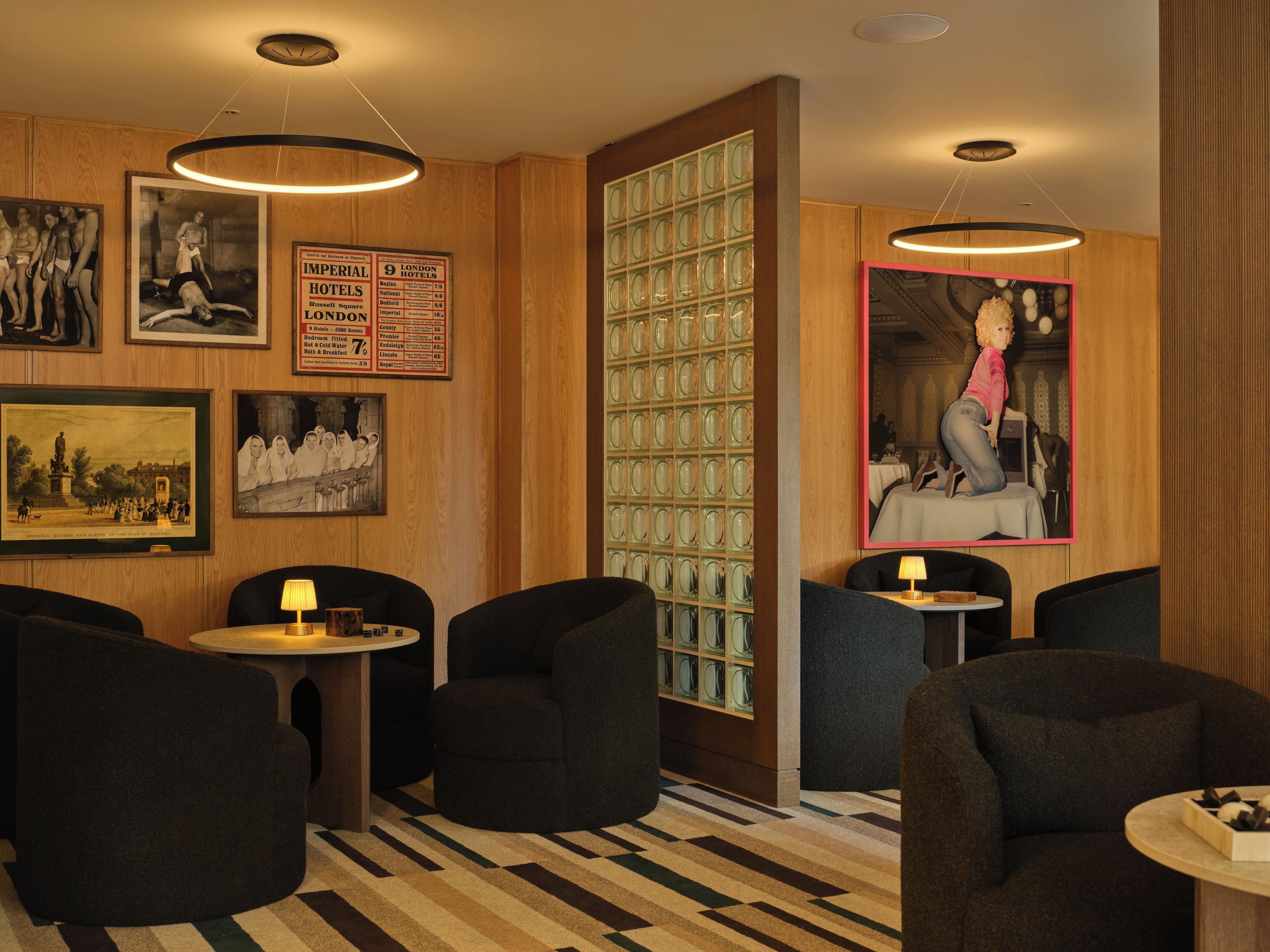 A hotel lobby with a checkered floor, black armchairs, a glass partition, and framed historical photographs.