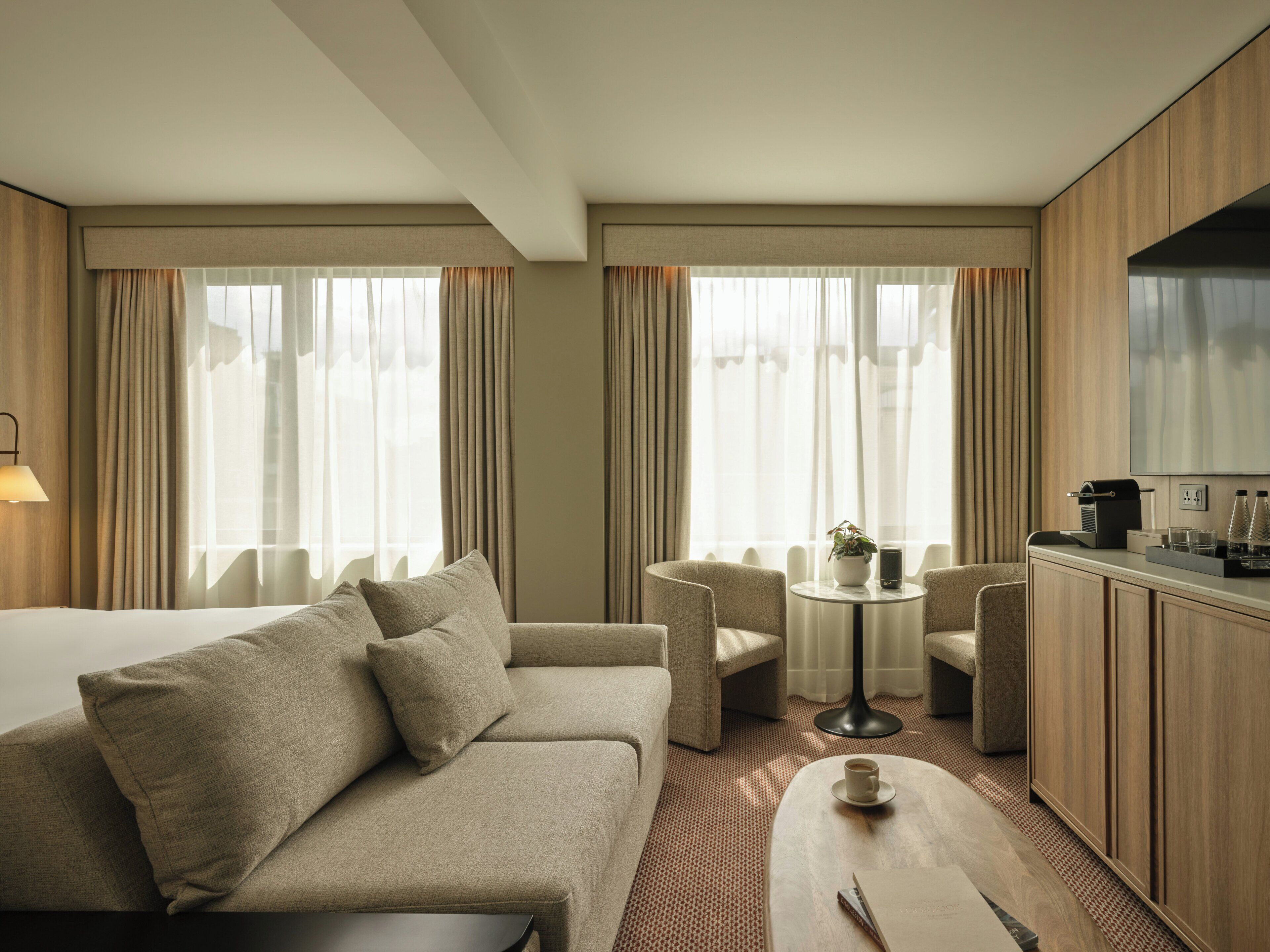 A hotel room with a bed, a sofa, a small round table, a coffee machine, and a TV.