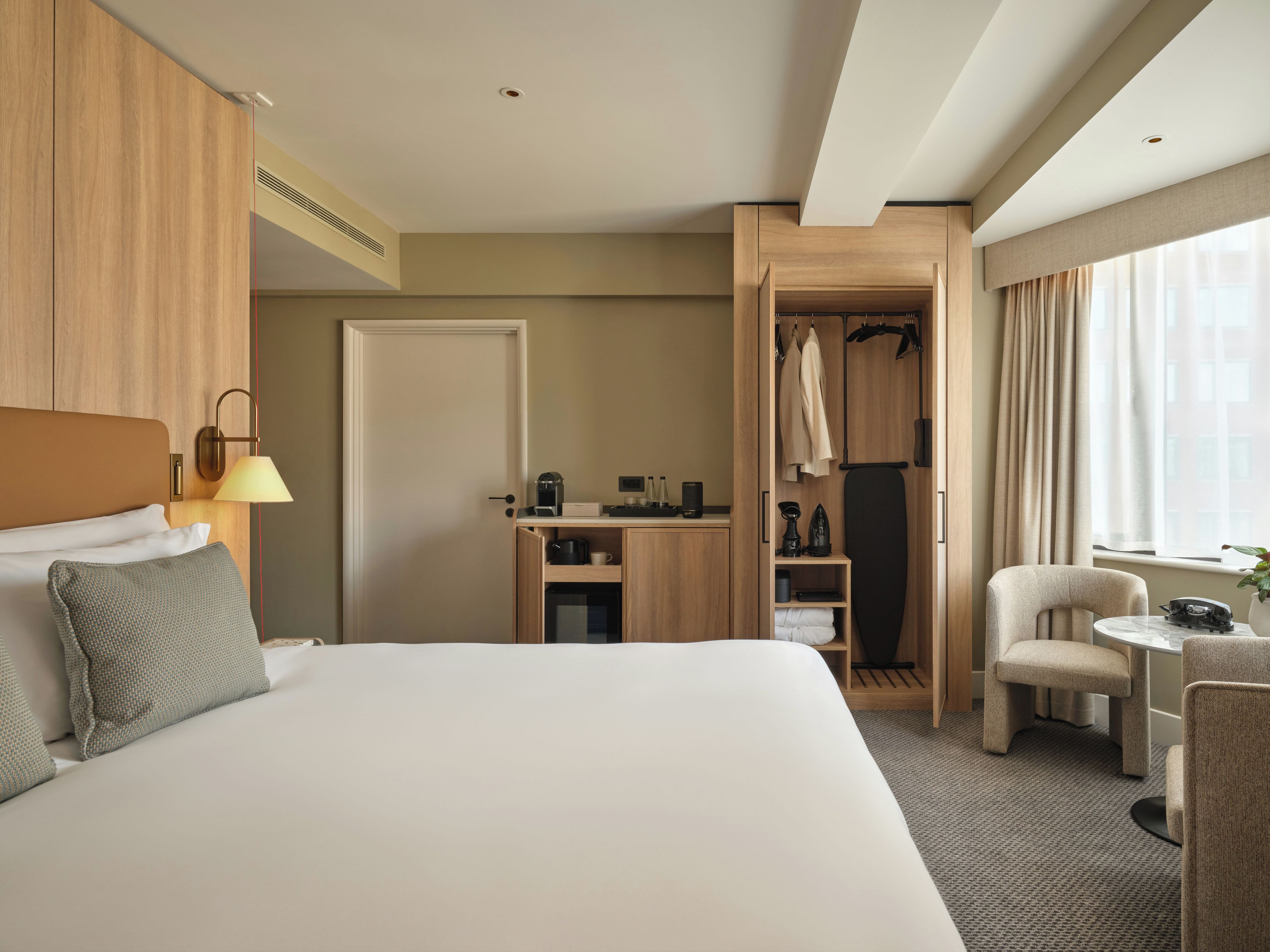 A hotel room with a large bed, a desk, a chair, a wardrobe, and a window with curtains.