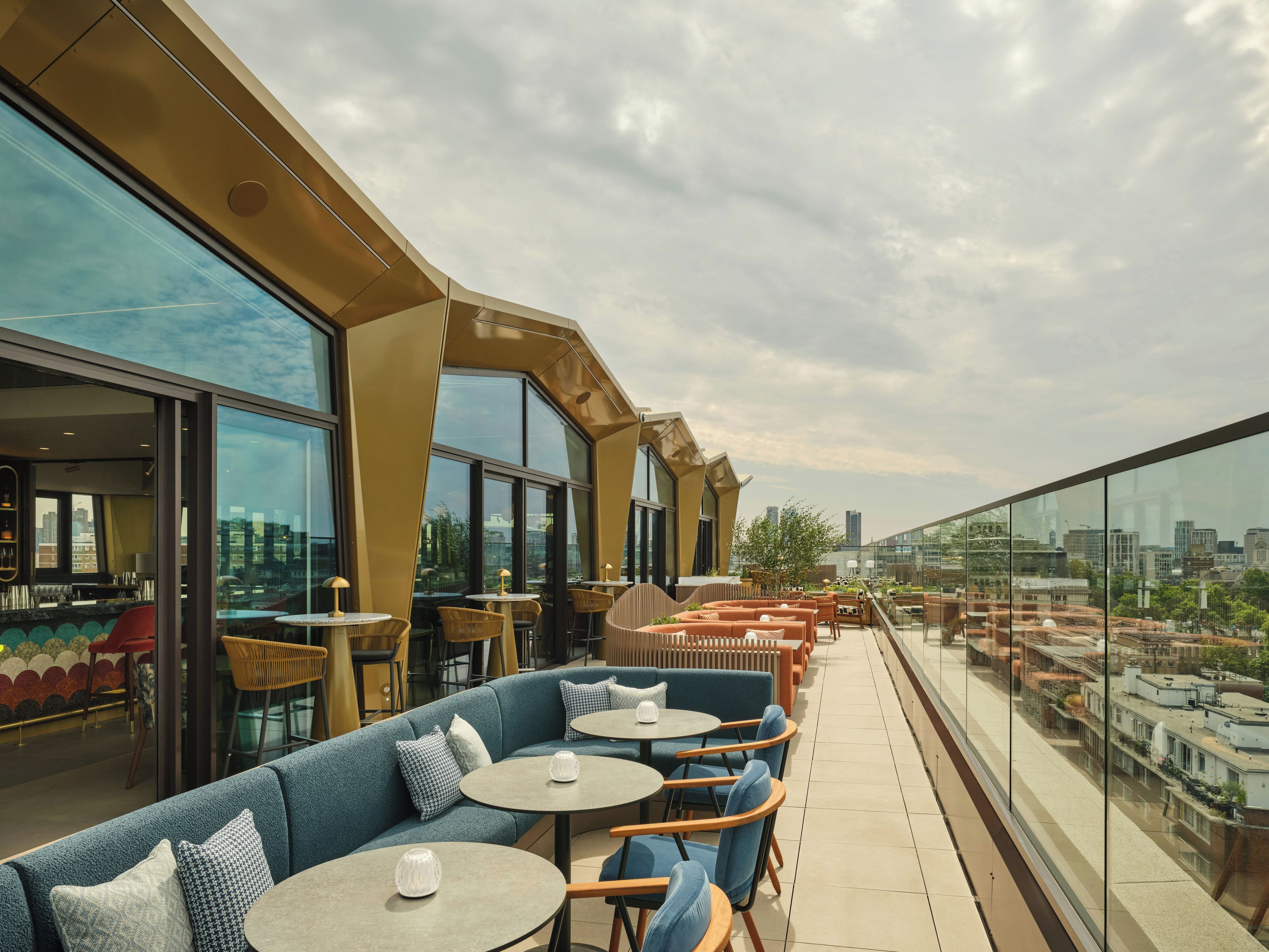 Eine Dachterrasse mit Sitzgelegenheiten im Freien und großen Fenstern, die einen Blick auf die Stadt ermöglichen.