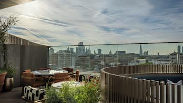 Una terraza en la azotea con vistas al horizonte de la ciudad, mobiliario y plantas en macetas.