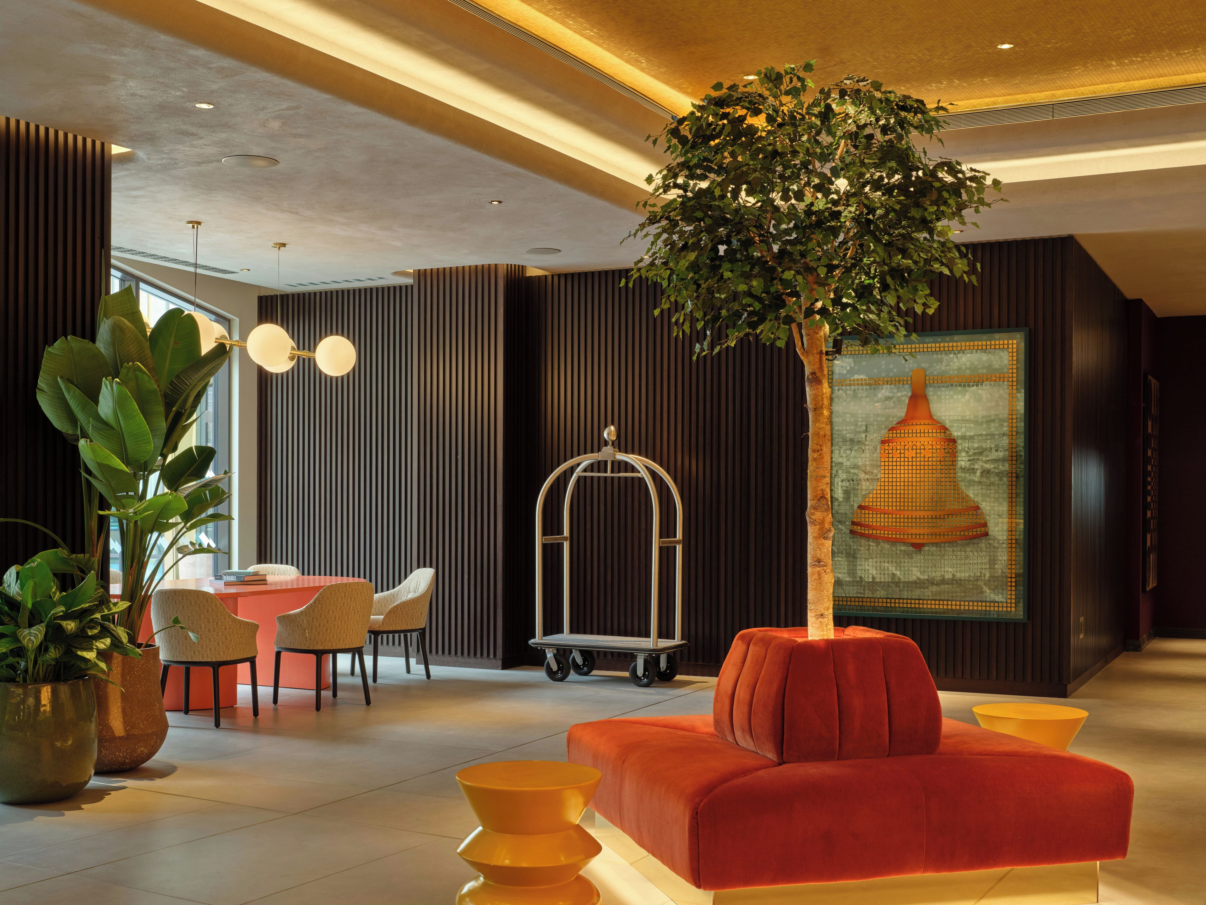 Un intérieur moderne avec un canapé rouge, des plantes en pot, un coin repas et une œuvre d’art accrochée au mur.