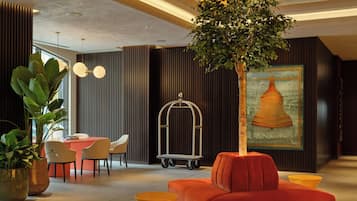 A modern interior with a red sofa, potted plants, a dining area, and a wall-mounted artwork.