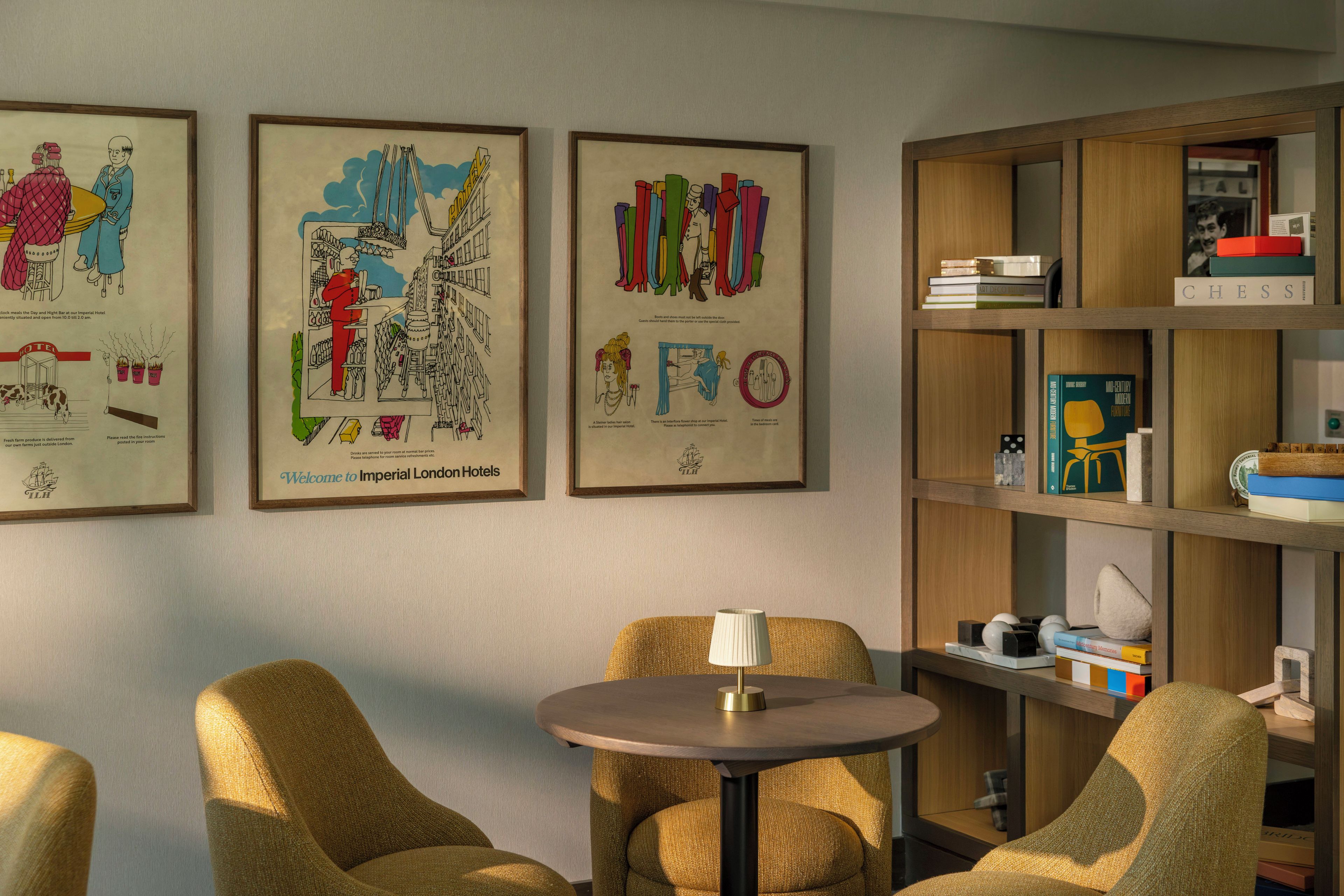 A hotel room with a round table, two armchairs, and a bookshelf with books and decorative items.