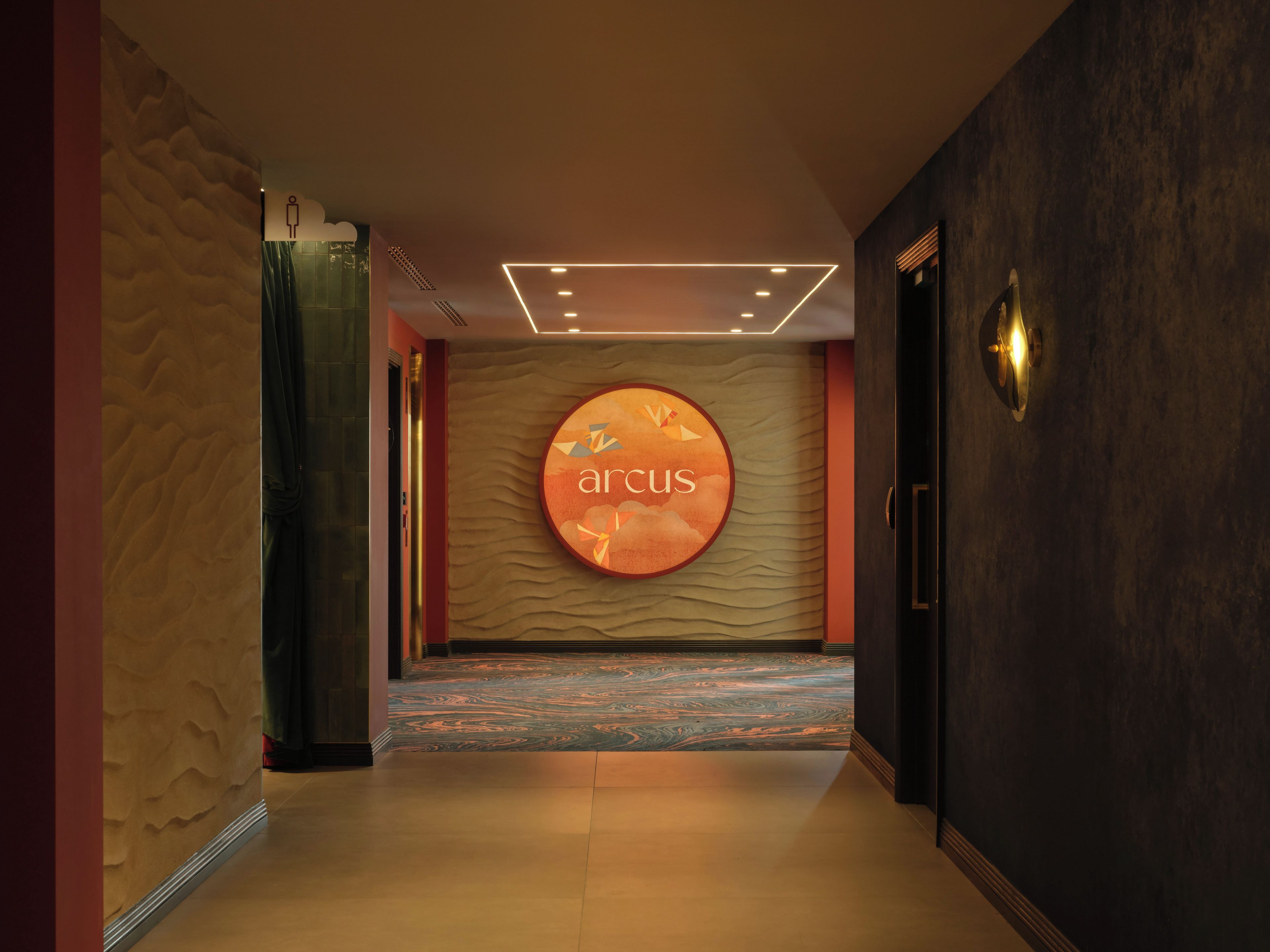 A hallway with a textured wall, a circular sign with the word 'arcus,' and a patterned carpet.
