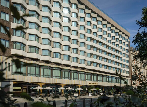 A multi-story hotel with a modern facade, large windows, and outdoor seating area. - The Imperial (London)