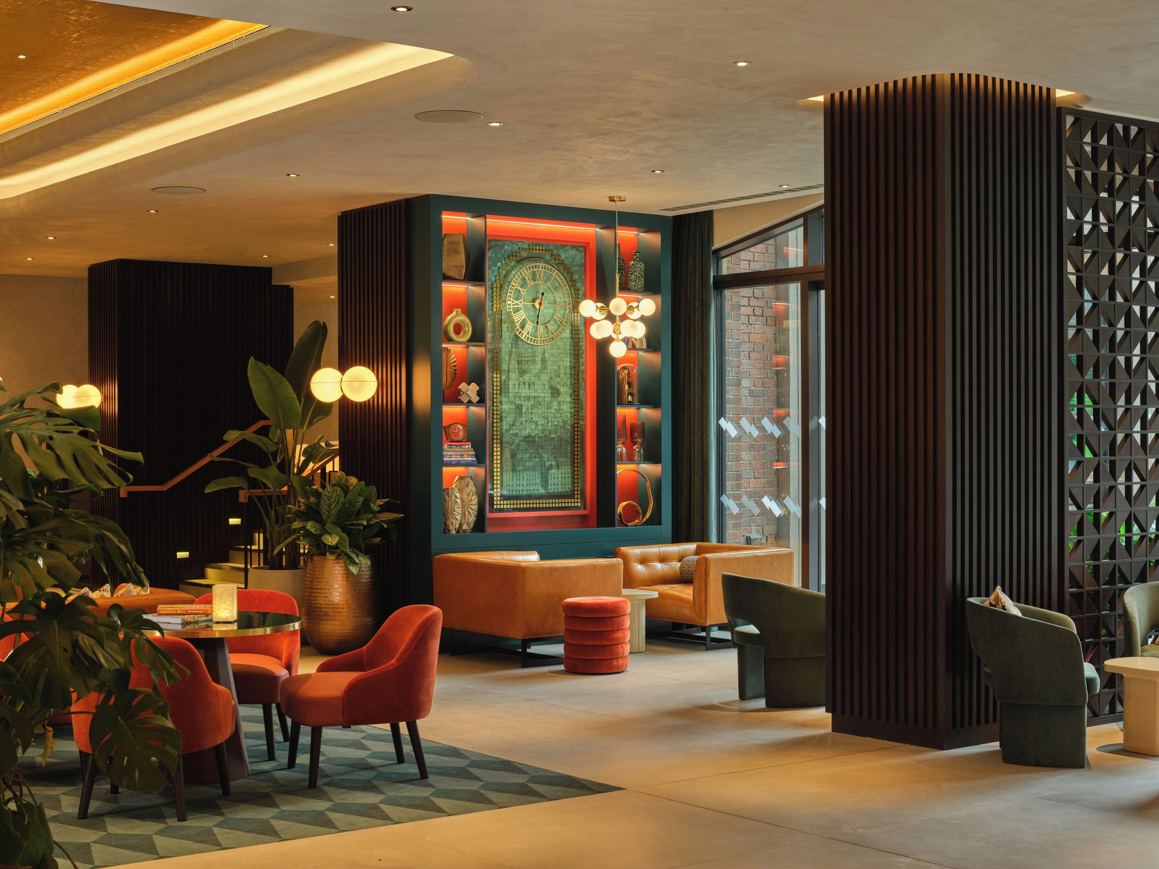 A modern lobby with seating areas, a decorative wall with a clock, and a large window.