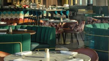 L’intérieur d’un restaurant avec des tables rondes, des sièges recouverts d’un tissu vert et un décor moderne.