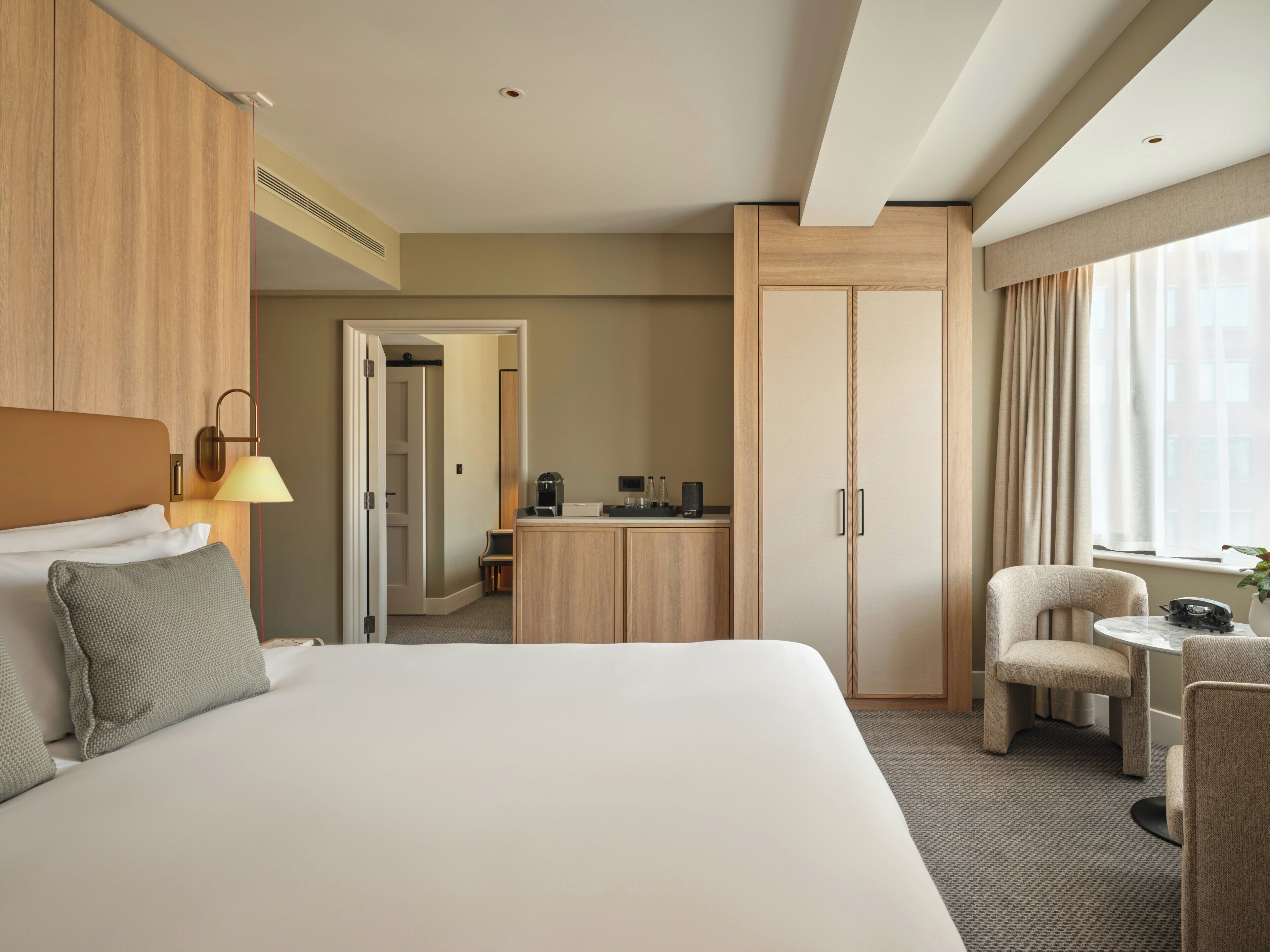 Habitación de hotel con una cama grande, un escritorio con silla, un armario y un baño visible a través de una puerta abierta.
