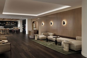 Un interior moderno con un sofá, una mesa de centro y sillas, una zona de cocina y una pared de madera con lámparas circulares.