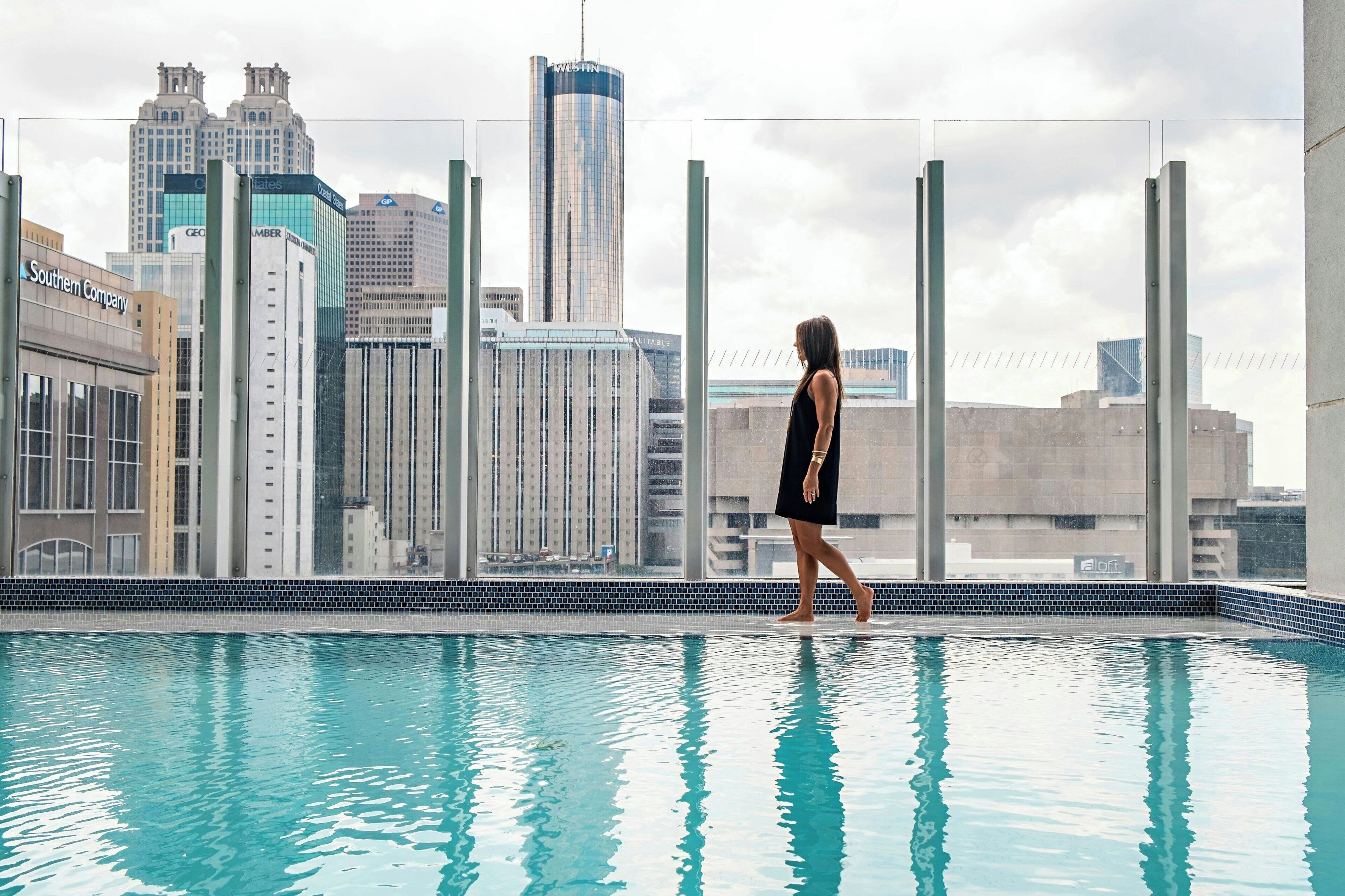A person walking by a pool with a city skyline in the background.