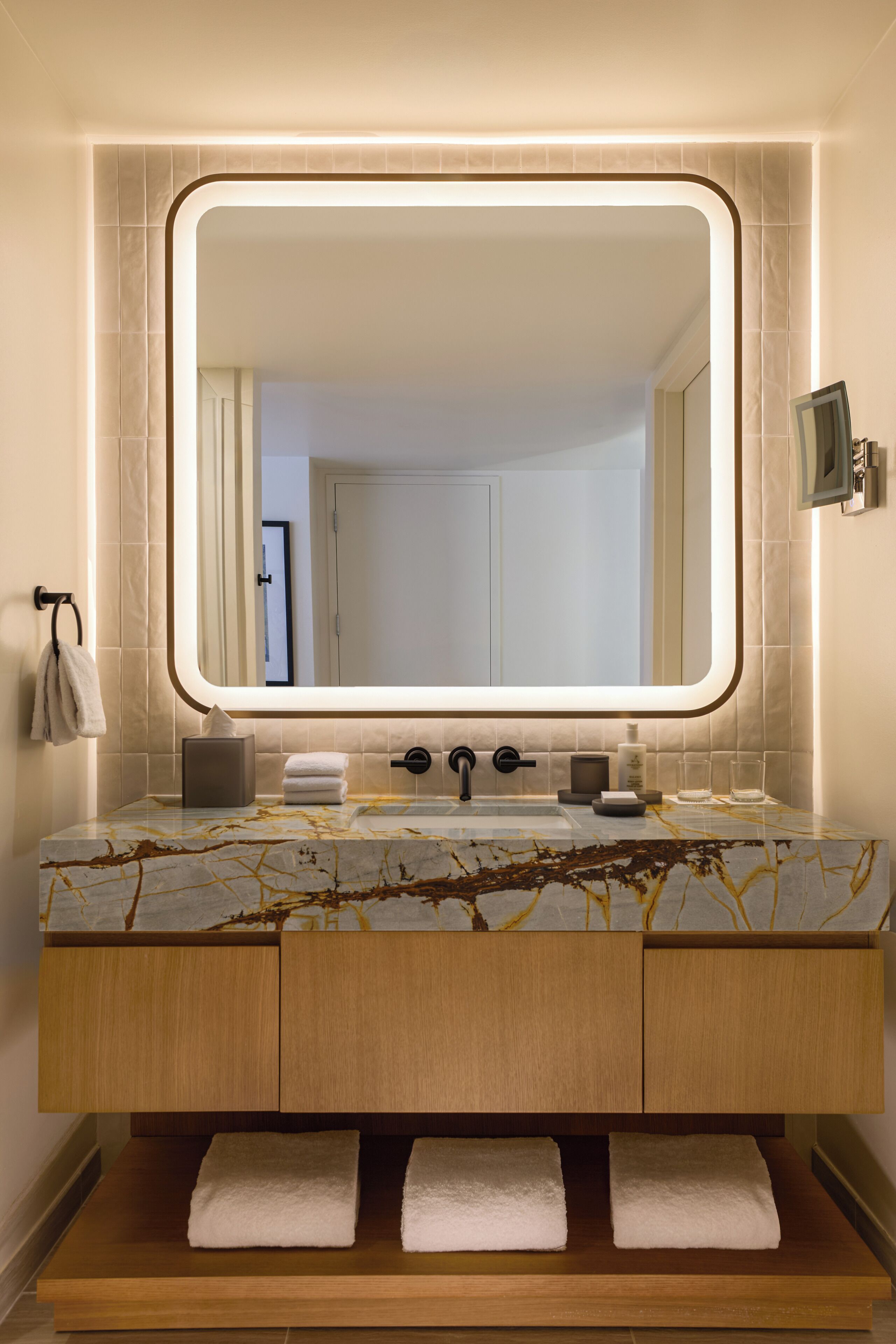 A modern bathroom with a large mirror, marble countertop, wooden vanity, and built-in towel racks.