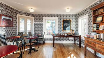 A dining area with patterned wallpaper, wooden flooring, and a central table with chairs.