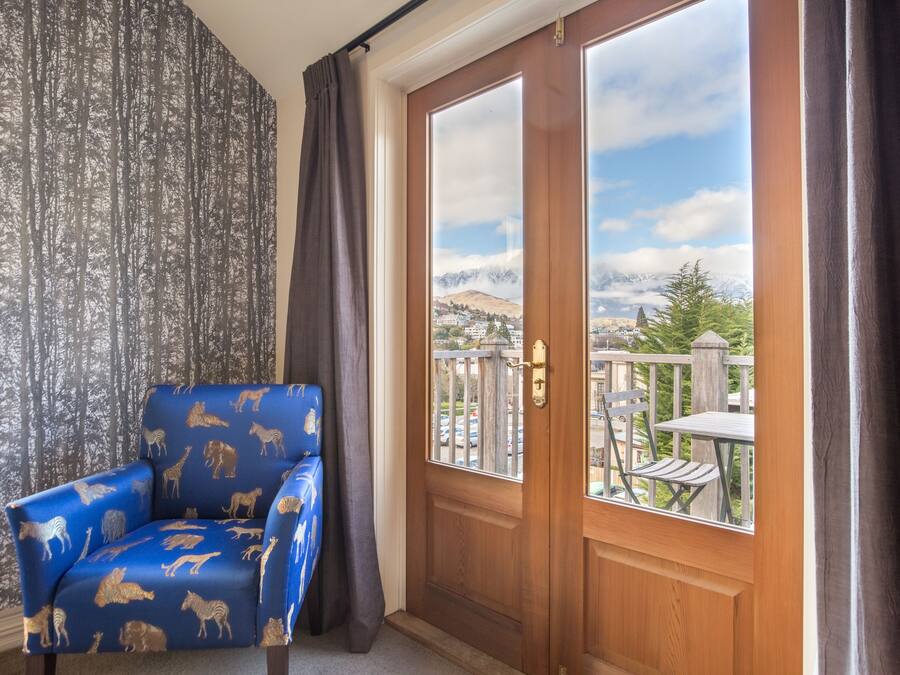 A room with a blue armchair featuring animal prints, a wooden door with a view of a balcony, and a patterned wallpaper.