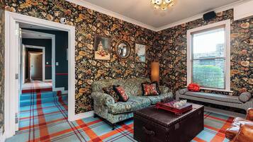 A room with a floral wallpaper, a sofa, a bench, and a patterned rug.