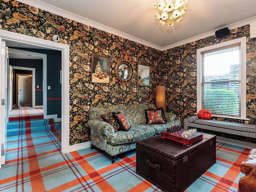 Una habitación con papel tapiz floral, un sofá, un banco y un tapete estampado.