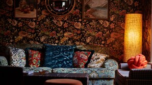 Un salon chaleureux avec un papier peint à motifs floraux, un canapé à motifs et une table sur laquelle se trouve une lampe.