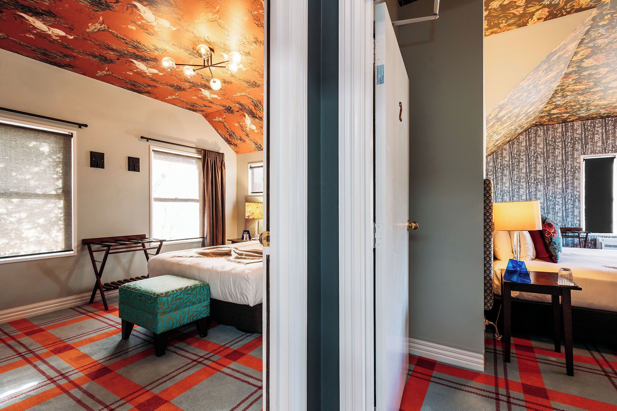 A room with a plaid carpet, a bed with a white duvet, a bench, and a table with a lamp.