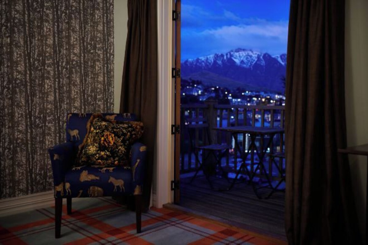 A room with a view of snow-capped mountains, a plaid-patterned carpet, and a blue armchair with a floral pillow.