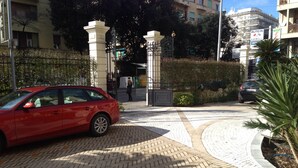 A red car parked in a paved area with a herringbone pattern, a gated entrance, and a building in the background. - Il Giardino di Albaro (Genoa)