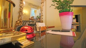 A hotel reception desk with a mirror, a red bell, a potted plant, a notepad, and a pen. - Il Giardino di Albaro (Genoa)