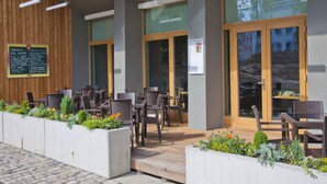 An outdoor seating area with wicker chairs and tables, a wooden wall, and a signboard listing menu items. - EA Business Hotel Jihlava (Jihlava)