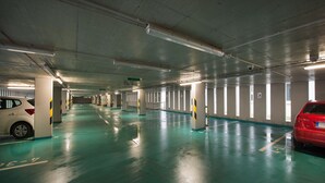 A multi-level parking garage with a wet floor, concrete pillars, and a red car parked on the right. - EA Business Hotel Jihlava (Jihlava)