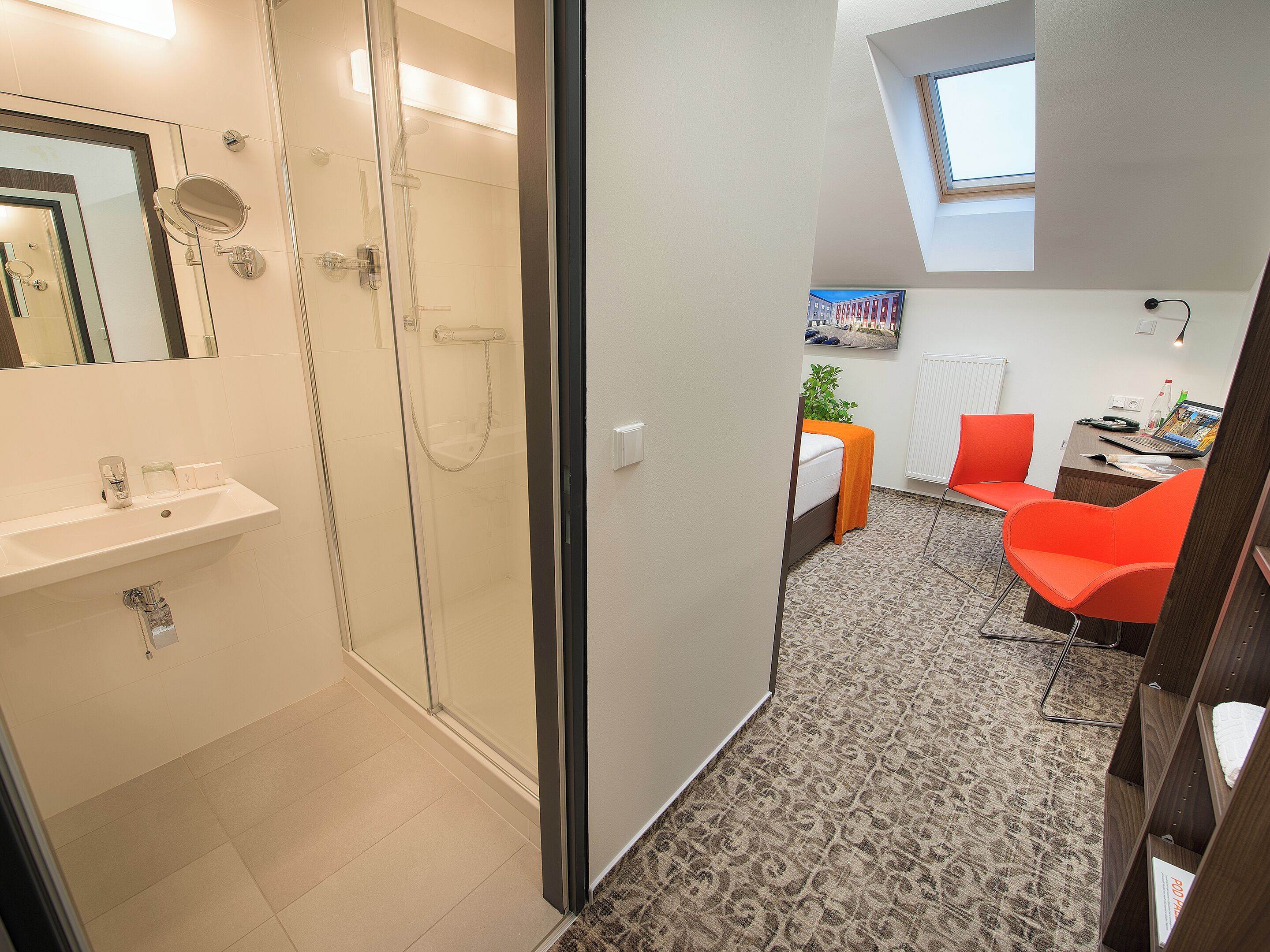 A modern bathroom with a glass shower enclosure, a sink with a mirror, and a small desk with a chair.