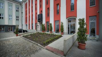 Un edificio con fachada roja y blanca, un patio empedrado con plantas en macetas y una entrada de adoquines.
