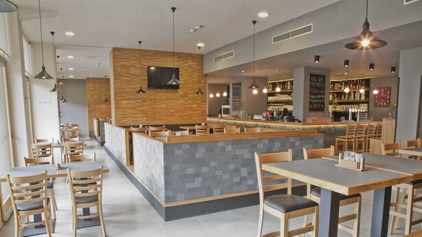 A modern restaurant with wooden tables and chairs, a central bar area, and pendant lighting. - EA Business Hotel Jihlava (Jihlava)