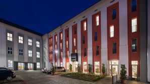 A multi-story hotel with a red and white facade, a cobblestone courtyard, and a car parked in front. - EA Business Hotel Jihlava (Jihlava)