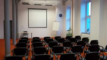 Un salón de conferencias con filas de sillas negras, una pizarra, una pantalla de proyector y un reloj en la pared.