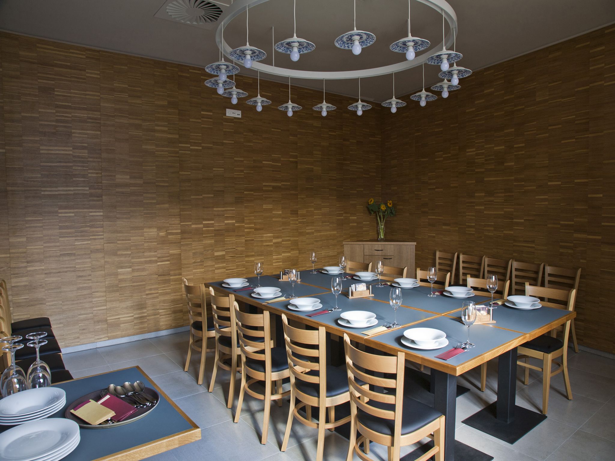 Un espace repas avec une longue table dressée pour accueillir plusieurs personnes, des chaises en bois et un lustre moderne.