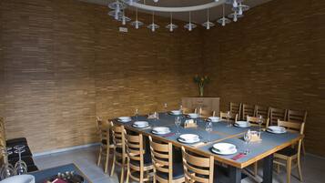Un espace repas avec une longue table dressée pour accueillir plusieurs personnes, des chaises en bois et un lustre moderne.
