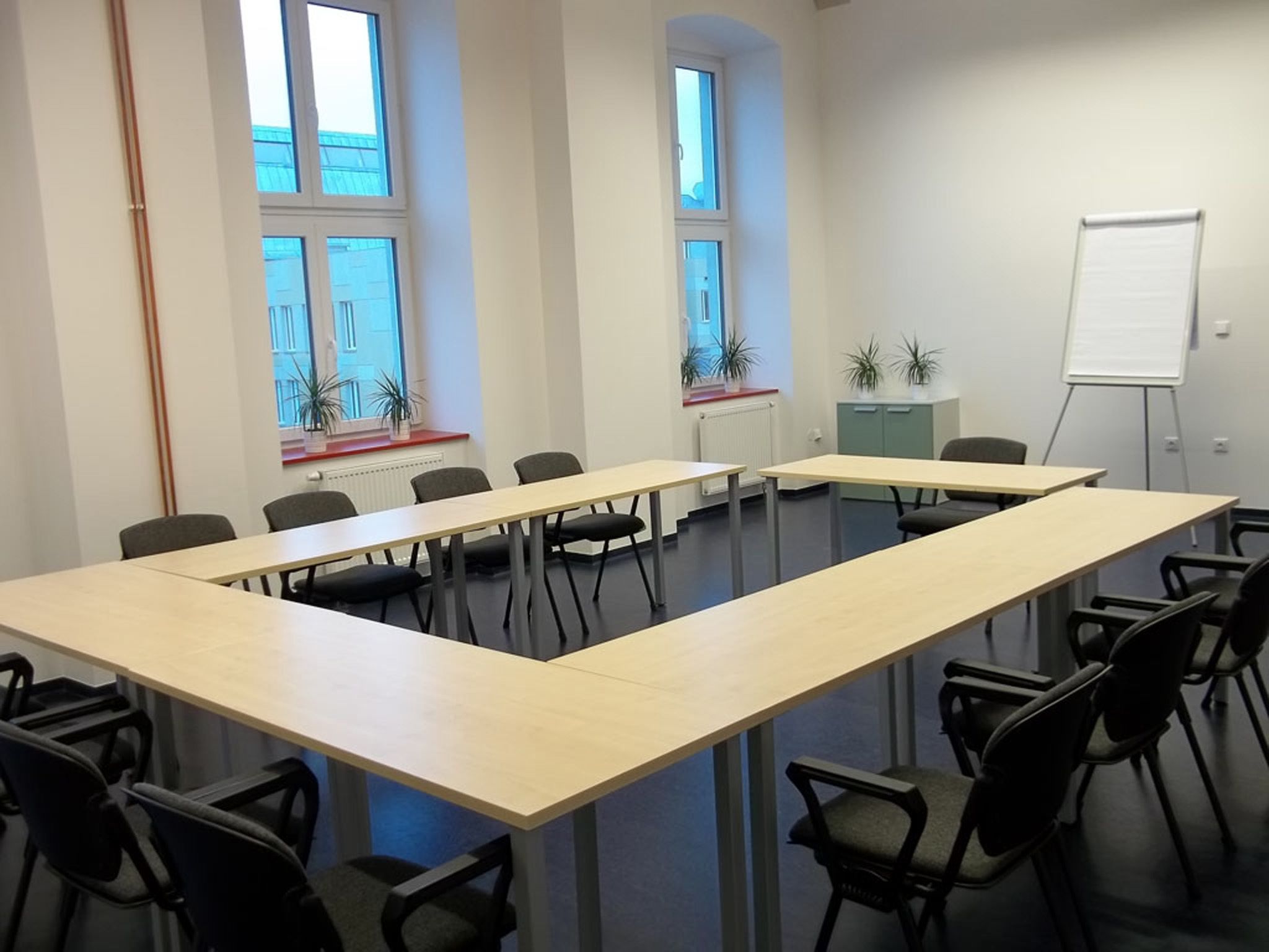 Ein Konferenzraum mit langem Tisch, Stühlen, einer Tafel und Fenstern mit Pflanzen.