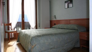 Un dormitorio con cama, una silla, una mesita de noche, un cuadro en la pared y una ventana con cortinas.