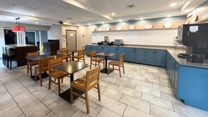 A restaurant with wooden tables and chairs, a kitchen area with blue cabinets, and a counter with a coffee machine. - Country Inn & Suites by Radisson, Port Charlotte, FL (Port Charlotte)