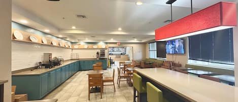 A modern restaurant with a long counter, multiple seating areas, and a kitchen visible in the background.