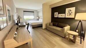 A modern hotel room with a bed, a sofa, a desk, and a small table. - Country Inn & Suites by Radisson, Port Charlotte, FL (Port Charlotte)