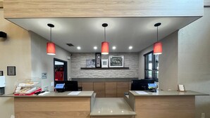 A reception area with a modern design, featuring a stone wall, wooden reception desk, and red pendant lighting. - Country Inn & Suites by Radisson, Port Charlotte, FL (Port Charlotte)