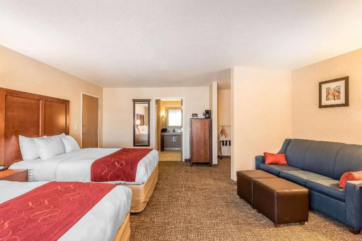 Habitación de hotel con dos camas, un sofá, un escritorio y un espejo.