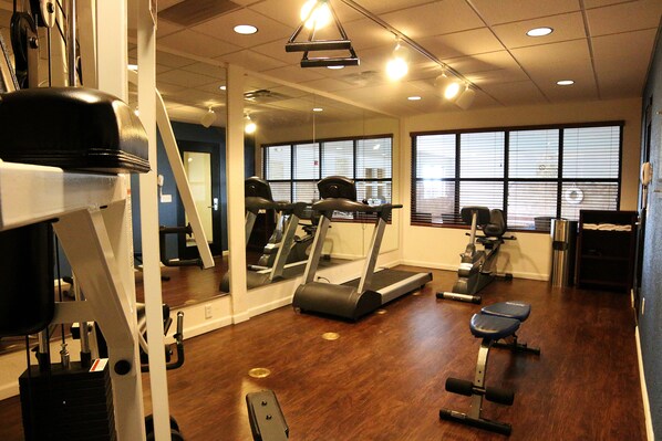 Un gimnasio con equipo de ejercicio, cinta de correr y banco para pesas.